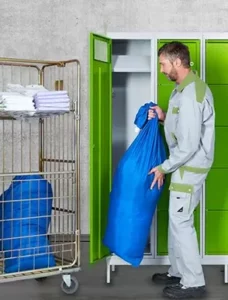 Mann, der Arbeitskleidung, die sich in blauen Säcken befindet, aus grünem Schrank holt und austauscht